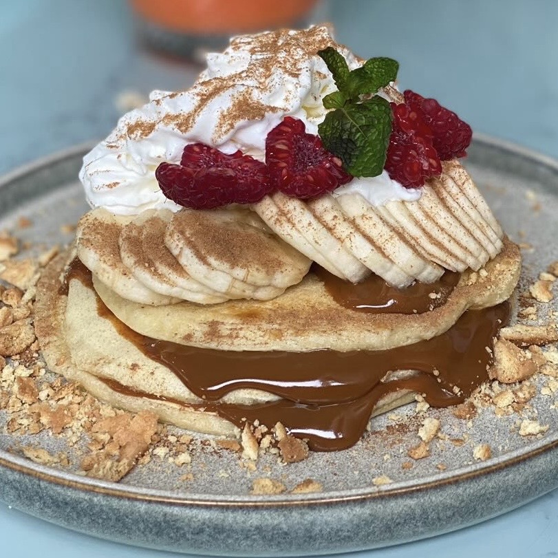 Três panquecas caseiras, framboesa, banana, doce de leite, natas frescas, crocante de bolacha, hortelã, canela